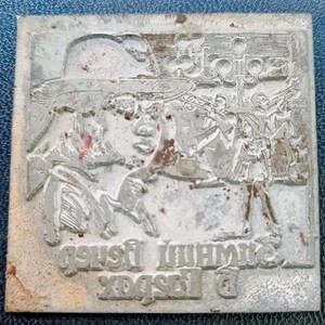 Puede incluir: Placa de impresión rectangular de metal plateado con una imagen en relieve detallada. La imagen representa a una persona con sombrero, un grupo de músicos y texto en la parte inferior. La placa tiene un aspecto desgastado y envejecido.