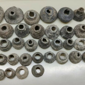 May include: A collection of 40 small, gray, ceramic, round, and cone-shaped beads with a hole in the center. The beads are arranged in rows on a white surface.