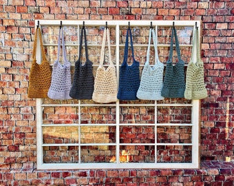 May include: Eight crocheted mesh bags in various colors hanging on hooks in a window frame. The bags are made of natural fibers and have a rustic, handmade look.