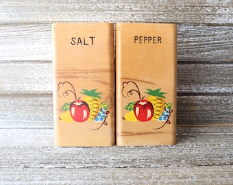 May include: Wooden salt and pepper shakers with a painted design of fruit, including apples, pineapples, and grapes. The shakers are labeled "SALT" and "PEPPER".