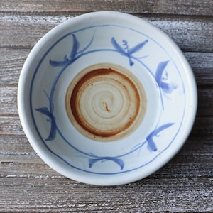 May include: A white ceramic bowl with a blue and white floral design. The bowl has a brown stain in the center.