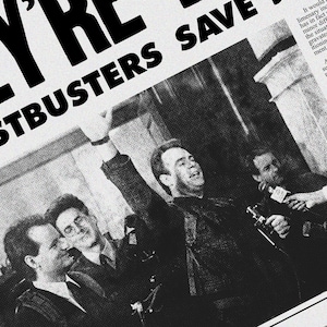 May include: A black and white photo of three men, one of whom is raising his arm in the air. The men are standing in front of a building with a sign that reads "Ghostbusters Save The Day".