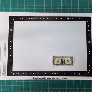 May include: A black rectangular frame with evenly spaced white dots, placed on a white surface. A one-dollar bill rests near the frame. The text "Don't forget to leave us a 5 star review!" is visible.