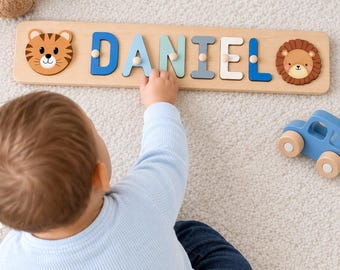 Puede incluir: Un rompecabezas de madera con el nombre DANIEL en letras coloridas, flanqueado por una cara de tigre a la izquierda y una cara de león a la derecha. Cada letra tiene un pequeño pomo de madera para agarrar sobre una base de madera clara.