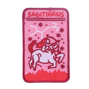 May include: Pink and red embroidered iron-on patch with the zodiac sign Sagittarius. The patch features a red and white illustration of a centaur holding a bow and arrow.