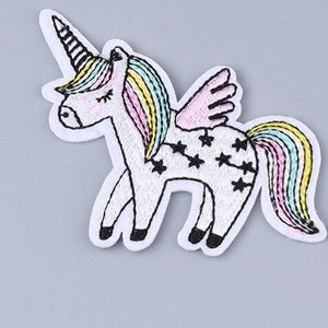 May include: A white embroidered unicorn with a rainbow mane and tail, pink wings, and black stars on its body.