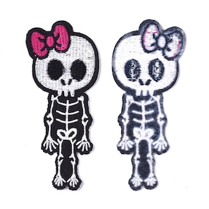 May include: Two embroidered iron-on patches of skeletons with bows. The skeleton on the left has a pink bow and the skeleton on the right has a white bow.