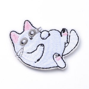 May include: Embroidered patch featuring a white cat lying on its back. The cat has pink ears and paws, gray eyes, and black whiskers. The patch is outlined in black.
