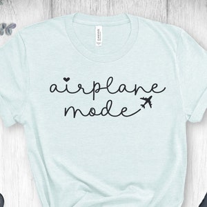 Puede incluir: Una camiseta azul claro con el texto "airplane mode" en letras negras. El texto incluye un peque&ntilde;o coraz&oacute;n y un icono de avi&oacute;n.