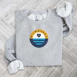 May include: Gray sweatshirt with a yellow, blue, and white circle graphic that says "MILWAUKEE WI" with a heart inside the circle.