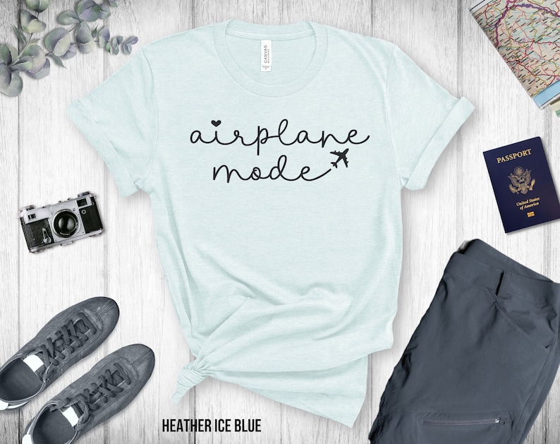 Puede incluir: Una camiseta azul claro con el texto "airplane mode" en letras negras. El texto incluye un peque&ntilde;o coraz&oacute;n y un icono de avi&oacute;n.