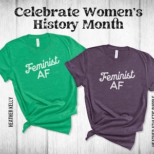 May include: Two t-shirts with the text "Feminist AF" in a white retro font. The shirt on the left is green and the shirt on the right is purple.