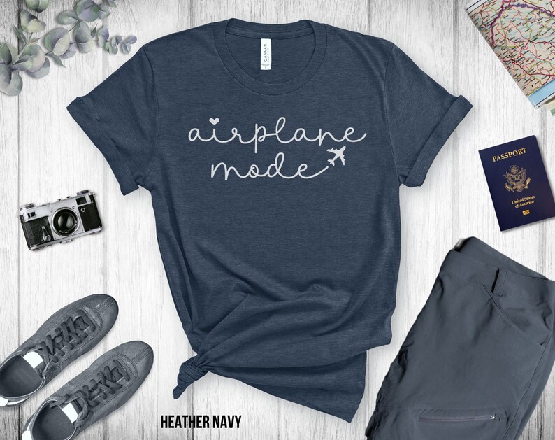 Puede incluir: Una camiseta azul marino jaspeada con el texto "airplane mode" en letras blancas cursivas. Un peque&ntilde;o coraz&oacute;n blanco y un icono de avi&oacute;n est&aacute;n por encima del texto.