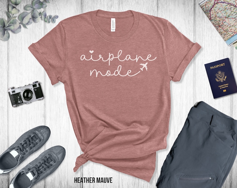 Puede incluir: Una camiseta de color malva con el texto "airplane mode" en letras blancas con un peque&ntilde;o coraz&oacute;n y un gr&aacute;fico de avi&oacute;n.
