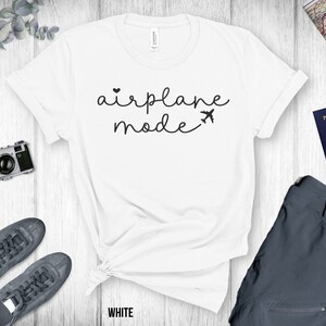 Puede incluir: Camiseta blanca con el texto "airplane mode" en escritura negra con un peque&ntilde;o coraz&oacute;n y un icono de avi&oacute;n.