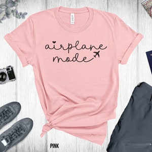 Puede incluir: Camiseta rosa con el texto "airplane mode" en letras negras con un peque&ntilde;o coraz&oacute;n y un gr&aacute;fico de avi&oacute;n.