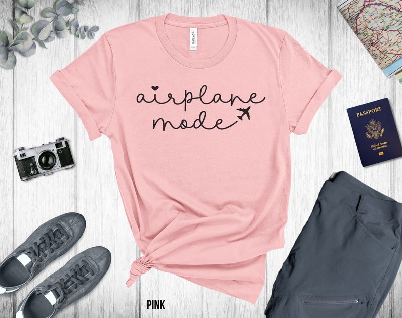 Puede incluir: Camiseta rosa con el texto "airplane mode" en letras negras con un peque&ntilde;o coraz&oacute;n y un gr&aacute;fico de avi&oacute;n.
