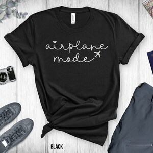 Puede incluir: Camiseta negra con texto blanco que dice "modo avi&oacute;n" y un peque&ntilde;o icono de avi&oacute;n.