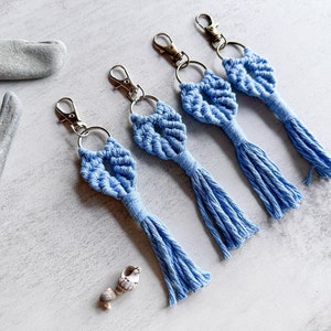 May include: Four light blue macrame keychains with silver key rings and tassels. The keychains are made with a knotting technique and have a diamond shape.