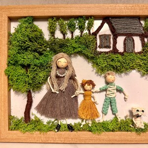May include: A framed yarn art piece depicting a family of three with a white cat and a small house in a green mossy forest setting. The figures are made of yarn and have painted faces.