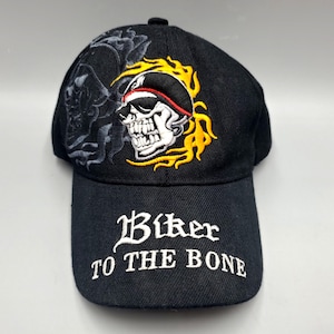 May include: Black baseball cap with embroidered skull and flames design. The cap features the text "Biker TO THE BONE" in white script on the front. A detailed biker-themed accessory.
