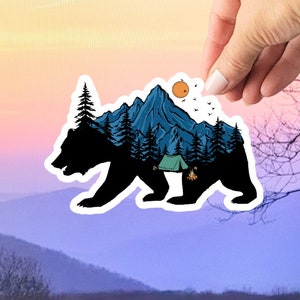 May include: A black bear silhouette with a mountain range, trees, a tent, and a campfire inside. The background is a sunset with a yellow sun.