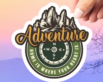May include: A green and brown compass with the words "Adventure Home is Where Your Heart Is" around it. The compass has a mountain range in the background.