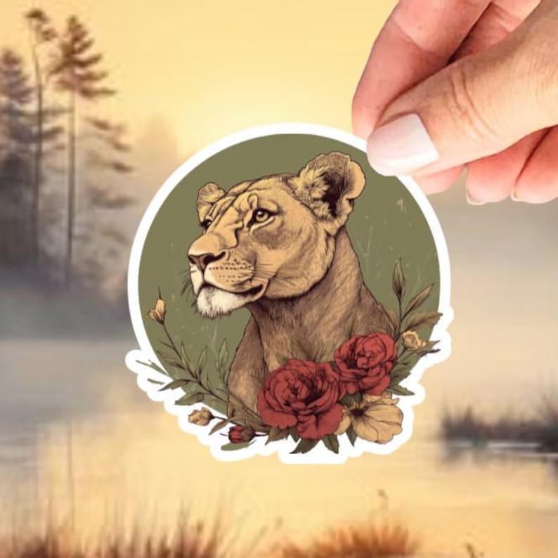 May include: A sticker featuring a detailed illustration of a lioness's head and shoulders, set against a green circular background. The lioness is brown with a detailed mane. Red roses and green foliage adorn the bottom of the sticker.