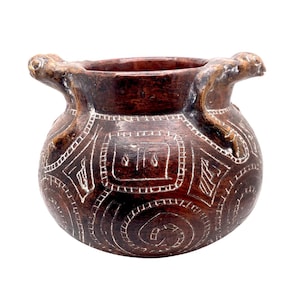 May include: A dark brown, handcrafted ceramic pot with a rounded body and two handles. The pot features intricate white etched patterns, including geometric shapes and spirals, creating a textured surface. The handles are sculpted with animal-like figures.