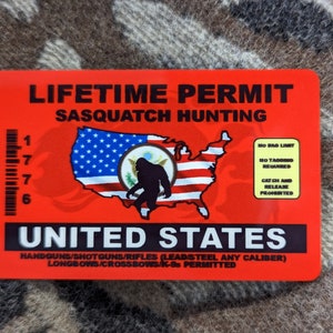 Puede incluir: Una tarjeta de plástico roja y negra con el texto "LIFETIME PERMIT SASQUATCH HUNTING" y un mapa de los Estados Unidos con un Sasquatch dentro del estado de Washington. La tarjeta también tiene el texto "UNITED STATES" y "HANDGUNS/SHOTGUNS/RIFLES (LEAD STEEL ANY CALIBER) LONGBOWS/CROSSBOWS/K-95 PERMITTED".