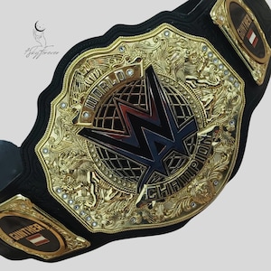 May include: A gold and black wrestling championship belt with intricate detailing. The belt features the WWE logo in the center, surrounded by the words "WORLD CHAMPION". The name "GUNTHER" is displayed on the side.