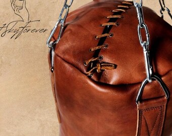 May include: A brown leather punching bag suspended by a silver chain. The bag features a central stitched seam and a leather strap attachment. The image includes the text "Skyforever" and a crescent moon and hand logo.