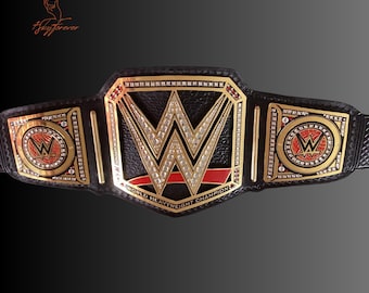 May include: A black and gold WWE World Heavyweight Championship belt. The belt features a large gold center plate with the WWE logo and the words "World Heavyweight Champion". The side plates also have the WWE logo.