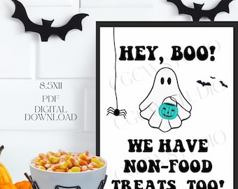 May include: Printable 8.5x11 inch PDF sign with a black frame, white background, and black text that reads "HEY, BOO! WE HAVE NON-FOOD TREATS, TOO!"  A cartoon ghost with two eyes and a mouth is holding a teal pumpkin. A black spider is hanging from a string above the ghost.