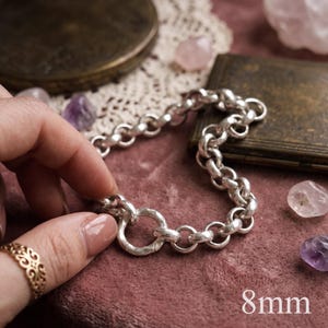 Könnte beinhalten: Ein silbernes Kettenarmband mit dicken, abgerundeten, ineinandergreifenden Gliedern und einer strukturierten Oberfläche. Das Armband verfügt über einen markanten runden Verschluss. Der Text 8mm ist unten rechts im Bild zu sehen.