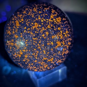 May include: A spherical, dark blue object with numerous small, orange-yellow spots. The sphere is resting on a clear, rectangular base, with a dark blue background. The overall effect is a glowing, cosmic appearance.