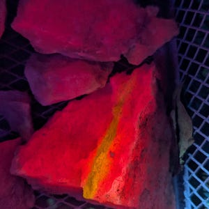 May include: Close-up of a red brick with a yellow streak running through it. The brick is illuminated with a pink and blue light, creating a vibrant and colorful effect.