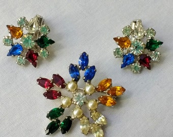 May include: A vintage jewelry set featuring a brooch and matching clip-on earrings. The brooch and earrings are designed with colorful, teardrop-shaped rhinestones in shades of red, blue, green, yellow, and orange, arranged around a central pearl and clear rhinestone.