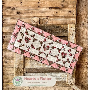 May include: A rectangular table runner featuring a patchwork design with three heart-shaped motifs. The fabric displays a floral pattern in shades of pink, brown, and white, with quilted textures. It measures 18 inches by 41.5 inches.