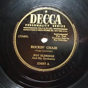 May include: A vintage black vinyl record with a gold and black label. The label reads "DECCA PERSONALITY SERIES" and features the song title "ROCKIN' CHAIR" by Roy Eldridge and His Orchestra. The record is a 78 RPM.