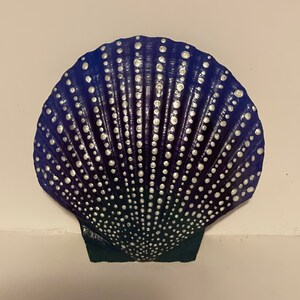May include: A purple seashell with a white dot pattern. The shell is painted with a gradient of purple and blue colors.