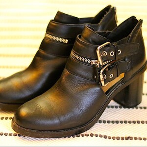 May include: Black leather ankle boots with cutouts and double buckles. The boots have a chunky heel and a zipper detail on the side.