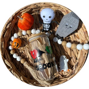 Könnte beinhalten: Ein klares Glasgefäß mit braunem Deckel und einem schwarz-weißen "I love Spook"-Design. Das Gefäß ist umgeben von einer weißen und braunen Perlenkette, einem kleinen orangefarbenen Kürbis, einem weißen Geist, einem grauen Sarg mit einem lächelnden Gesicht und einem weißen Skelett mit schwarzen Knochen.