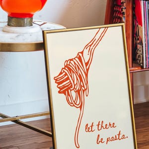 May include: A framed print with a white background and a red illustration of spaghetti on a fork. The text "let there be pasta." is written in red below the illustration.