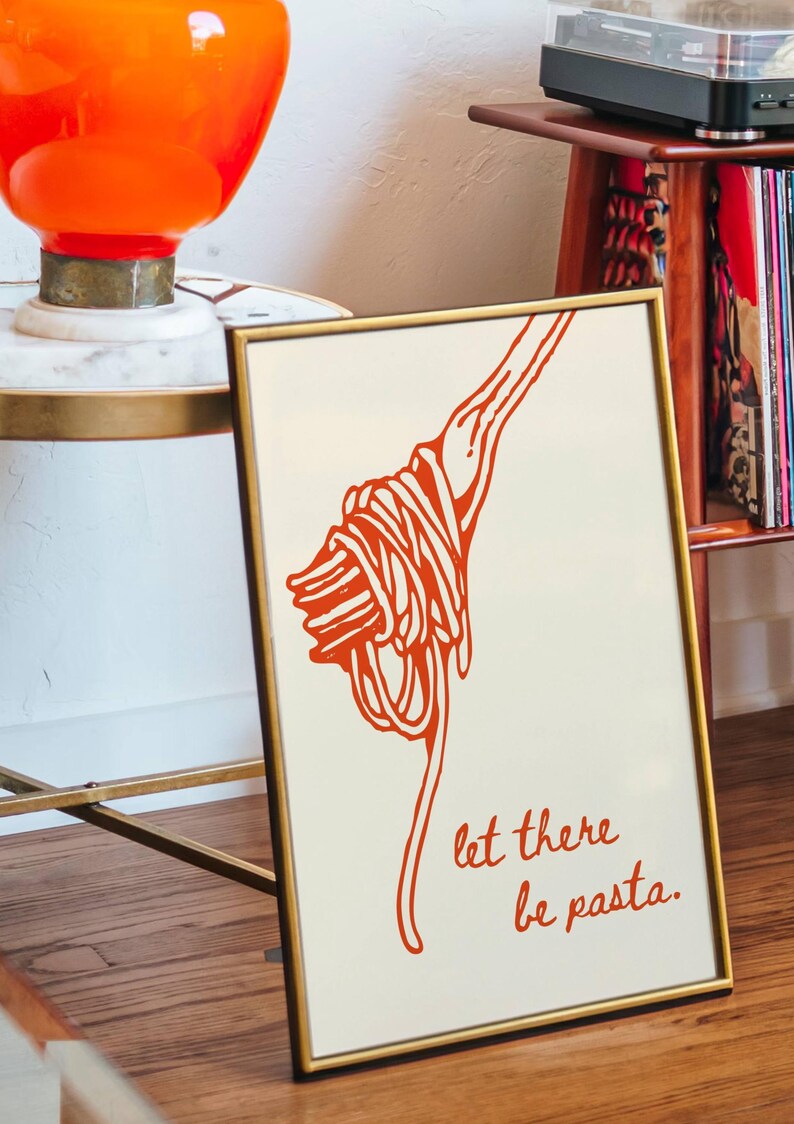 May include: A framed print with a white background and a red illustration of spaghetti on a fork. The text "let there be pasta." is written in red below the illustration.