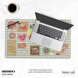 May include: A large, green and white checkered desk mat with various colorful, cartoonish patches. A laptop, coffee cup, and glasses are on the mat. The mat has the text "DESIGN 1" and "SIZE LARGE".