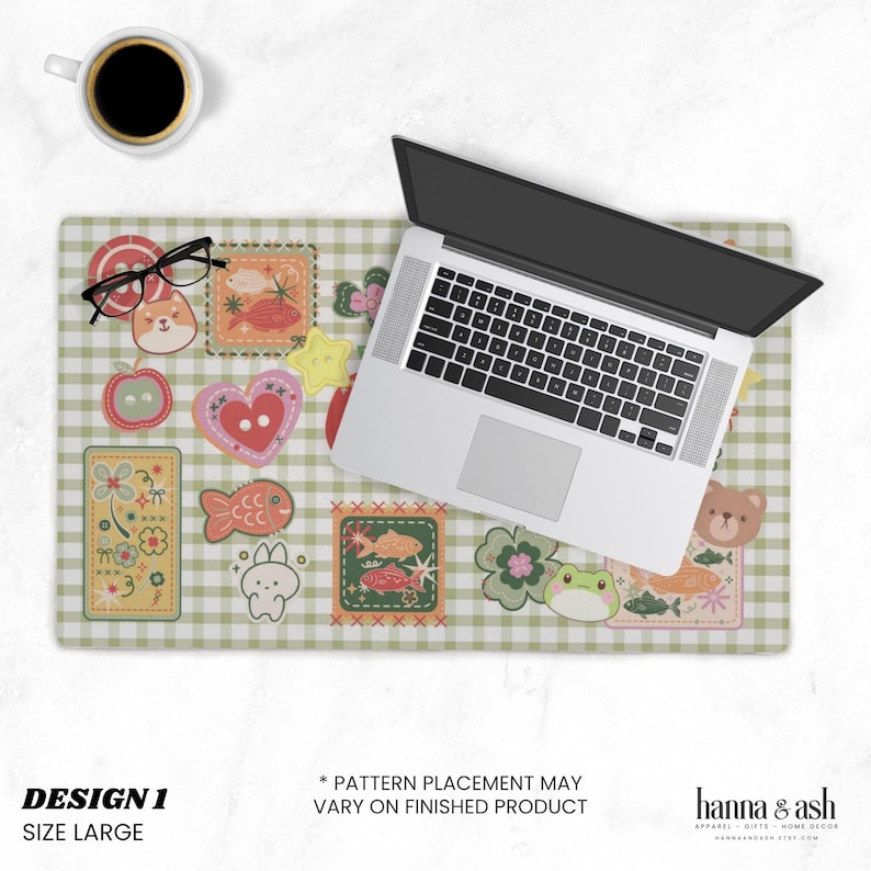 May include: A large, green and white checkered desk mat with various colorful, cartoonish patches. A laptop, coffee cup, and glasses are on the mat. The mat has the text "DESIGN 1" and "SIZE LARGE".