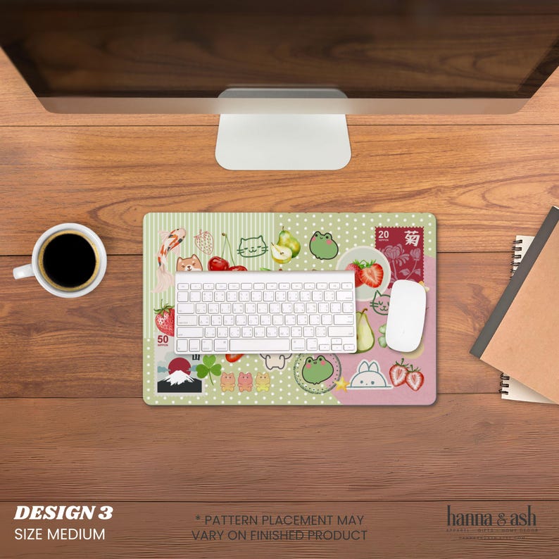 May include: A medium-sized, rectangular mousepad with a whimsical design featuring cartoon cats, frogs, strawberries, and other illustrations. The background is a mix of green stripes and pink polka dots. A white keyboard and mouse sit on the pad.