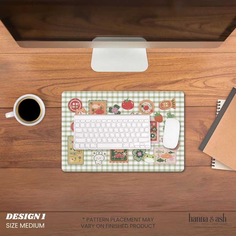 Pu&ograve; includere: Un tappetino per mouse di medie dimensioni con un motivo a quadri verdi e bianchi, con varie simpatiche illustrazioni. Una tastiera e un mouse bianchi sono sul tappetino, con una tazza di caff&egrave; e un taccuino nelle vicinanze. Testo "DESIGN 1 SIZE MEDIUM".
