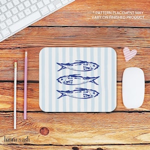 Puede incluir: Una alfombrilla de ratón a rayas azules y blancas con un diseño de tres peces azules sobre un fondo blanco. El texto "*PATTERN PLACEMENT MAY VARY ON FINISHED PRODUCT" está impreso en negro en la parte superior de la alfombrilla de ratón.